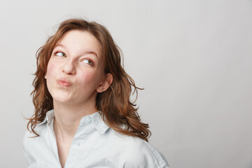 Young woman with red hair and fair skin looks thoughtfully to the side with pursed lips. Casual...