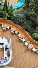 Fototapeta premium Modern cafe interior with wooden tables, chairs, curved bench, lush green plants, and a bar