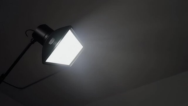 A bright softbox light shines on a dark background in a studio setting.