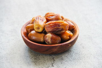 Obraz premium Ripe dates in a wooden plate on a gray concrete background, healthy natural sweet fruit commonly eaten during Ramadan