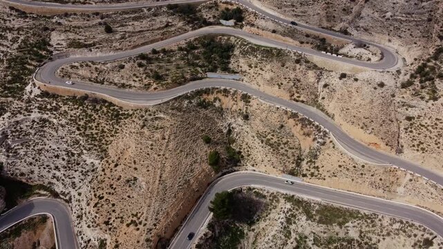 Aerial 4K drone top-down shot of cars driving along a winding zigzag mountain road in Alcal&aacute; del J&uacute;car, Spain. Cinematic view of a serpentine switchback road through a rugged canyon landscape