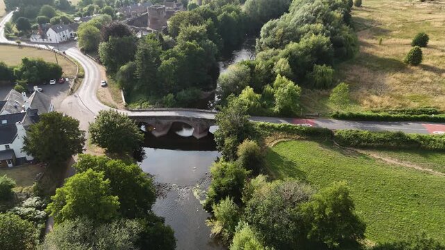 Skenfrith Castle Herefordshire,high view of the river and ancient bridge alongside the Norman Castle on the Welsh border with birds flying by in bright summer sunshine
