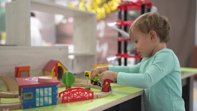 Young child playing with toy train. Boy, plays, railroad, toys carriages, train, son. A train with carriages and a boy playing with it. The photo is of a child playing lifestyle with a toy train.