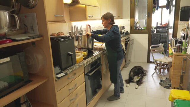 Woman preparing a meal in the kitchen while her dog waits