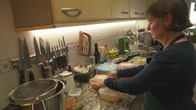 Mature woman storing leftover food in containers