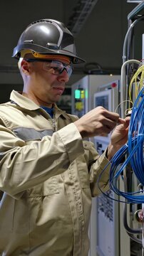 Industrial technician working on electrical control panel with network cables, vertical footage