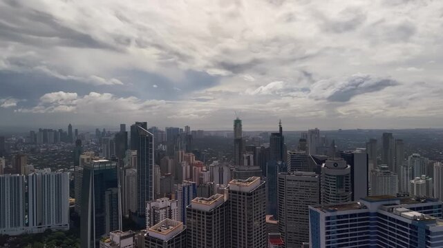 Drone glide beside Makati skyscrapers reveals rooftop structures and construction cranes above the business district and surrounding skyline layers under diffused daylight and heavy cloud cover