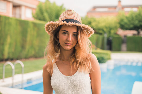Portrait of young woman with straw hat and swimsuit, pool in the background