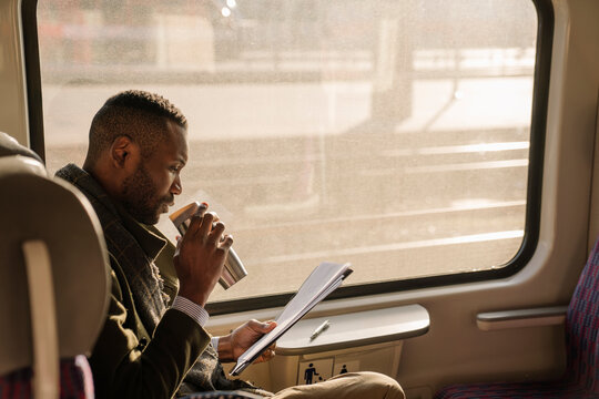 Stylish businessman with reusable cup and documents in a train