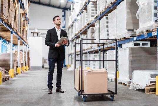 Businessman in warehouse loading cardboard boxes on transport cart