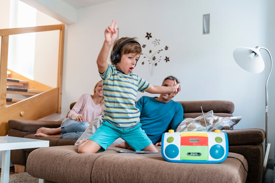 Excited boy listening to music with headphones on couch at home with parents in background