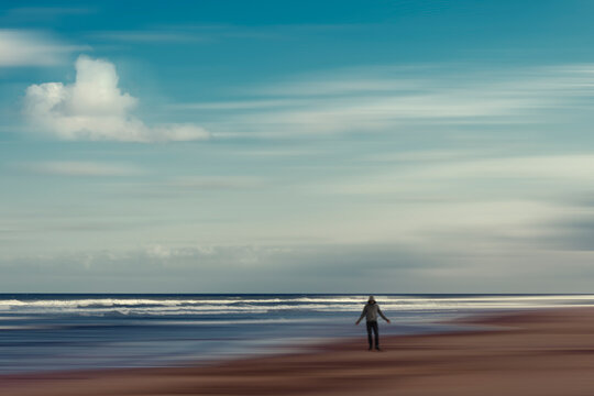 France, Nouvelle-Aquitaine, Contis, Clouds over hooded man standing on Contis Plage beach