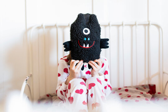 Little girl sitting in bed hiding face behind her soft toy
