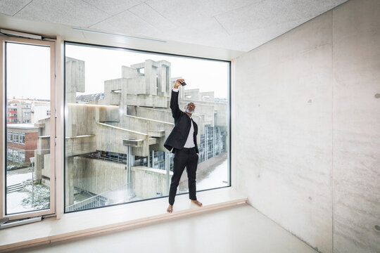 Barefoot businessman standing in front of window taking selfie with smartphone