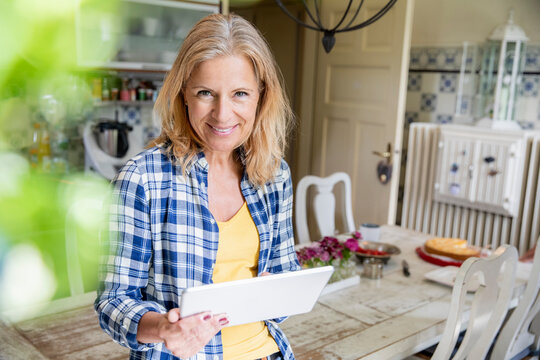 Portrait of smiling mature woman with digital tablet in the kitchen