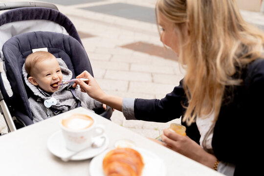 Mother feeding laughing baby boy in stroller