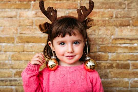 Portrait of smiling toddler girl wearing reindeer antlers headband and Christmas baubles