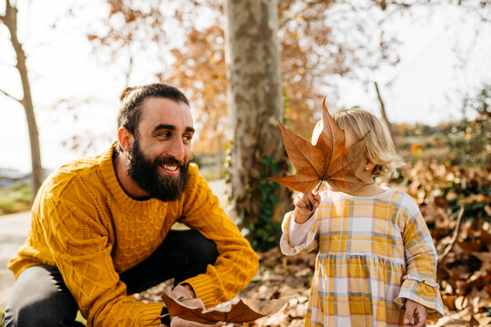 Father and daughter enjoying a morning day in the park in autumn, playing with autumn leaves