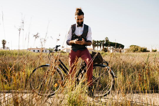 Well dressed man with his bike on a wooden walkway in the countryside using cell phone
