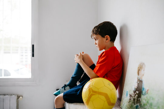 Sad boy with soccer ball sitting on sideboard