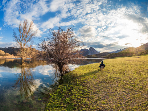 Spain, Asturias, Camposolillo, Cantabrian Mountains, senior man sitting at seashore of Porma reservoir enjoying the sunshine
