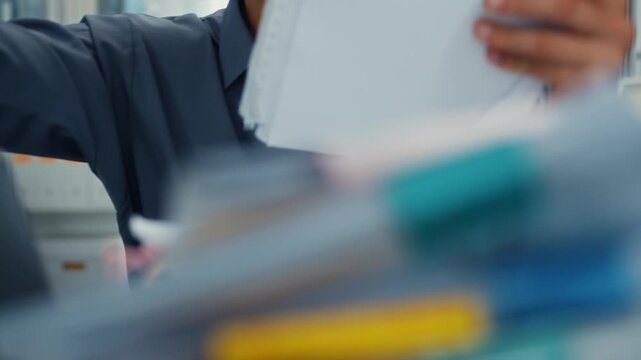 Closeup overworked young Latin businessman reading document in large stack of paperwork file at office desk. Tax audit deadline, accounting stress, corporate burnout, bookkeeping, bureaucracy concept.