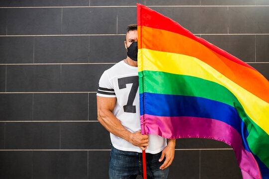 Young man wearing mask holding rainbow flag while standing against wall