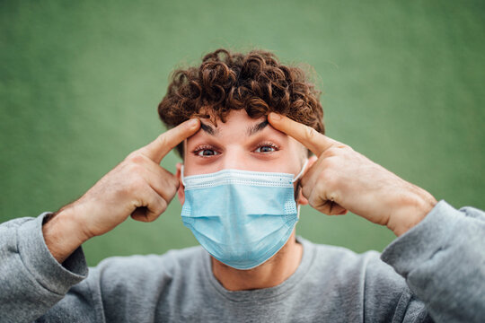 Young man touching eyebrows against green background in studio during COVID-19