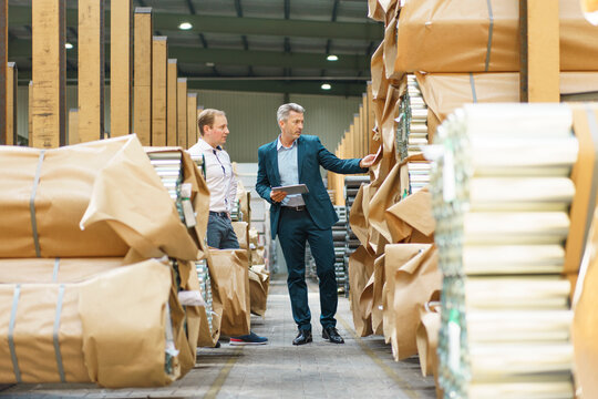 Two businessmen in a factory storehouse with steel pipes