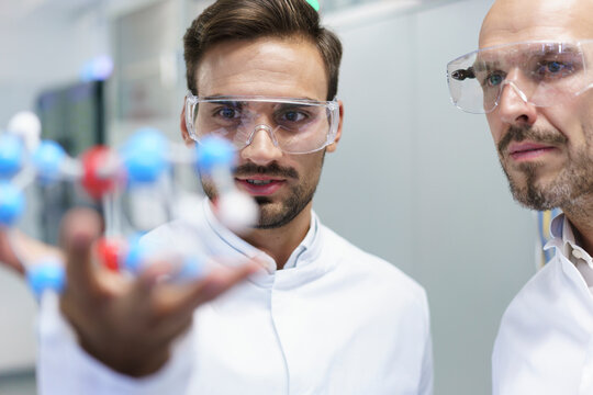 Confident male scientists analyzing molecular structure at illuminated laboratory