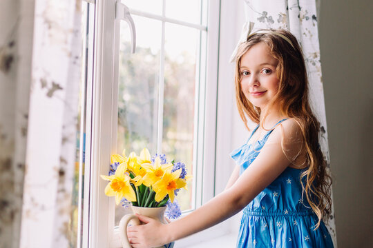 Portrait of smiling girl with flower vase of daffodils and hyacinths at home