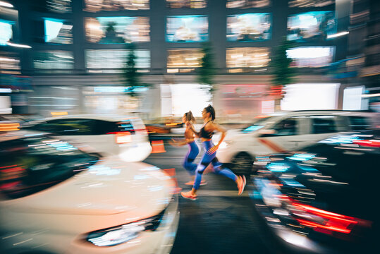 Long exposure photo of two women running through the streets in the city at night