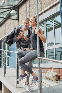 Portrait of mature man with sports bag and young woman in front of gym watching something