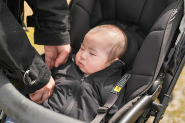 Softly sleeping baby in black stroller. Parent gently adjusts baby's jacket. Baby's calm expression conveys peace. Image captures quiet, tender moment. Perfect for parenting, family, or travel themes © Masakazu Tokashiki