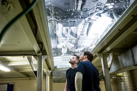 Two colleagues in factory checking underbody of a car
