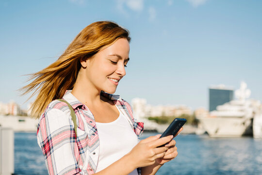 Woman text messaging on smart phone while standing at seaside during sunny day