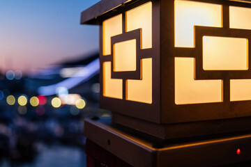 Warm glowing geometric lantern illuminates a serene evening. Urban bokeh lights create a peaceful atmosphere, perfect for design or travel themes © serebryannikov