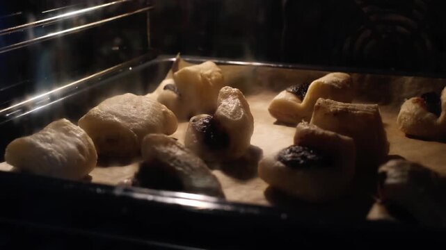 Fast motion of baking leaf fat pastry in an oven. Tray of traditional Hungarian lard dessert with plum jam rises behind a dirty oven glass as the dough expands in hot air. Grandma&rsquo;s kitchen concept.