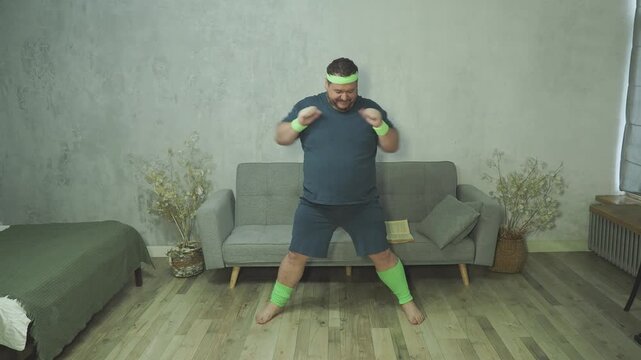 Overweight man lifting knees up and out to sides in funny home fitness workout. Chubby active person doing physical exercises, cardio or warmup training in living room. Happy fay man
