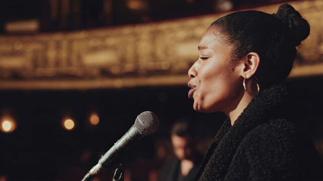 Side view of female jazz singer performing soulful vocal into microphone on warmly lit stage capturing expressive live performance mood during an intimate live performance