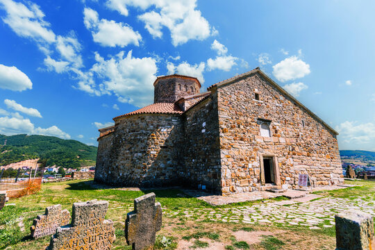Historic medieval stone church surrounded by an old cemetery with carved stone crosses under a bright blue sky Novi Pazar, Serbia