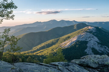 Fototapeta premium Scenic mountain landscape at sunrise with rocky ridge, lush green slopes, and distant peaks under a cloudy sky, perfect for travel, nature, and adventure projects.