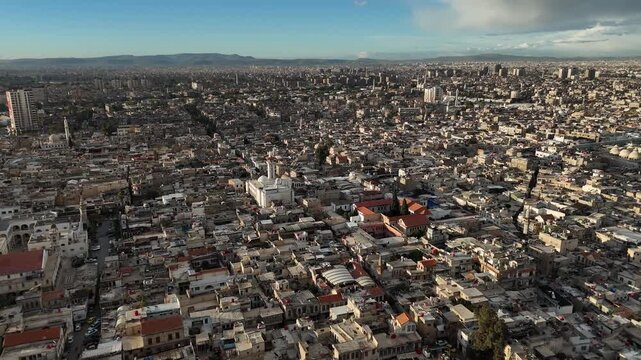A wide aerial drone shot over Damascus, Syria, featuring the historic Umayyad Mosque and the dense rooftops of the ancient Old City center