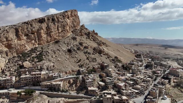 aerial drone of ancient settlement of Ma'loula, Syria, featuring the contrast between the stone architecture and the vast, barren mountain landscape