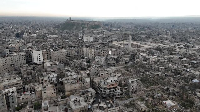 drone shot over war-torn Aleppo, Syria, showing the historic Great Mosque and the Citadel on the horizon amid extensive urban ruins