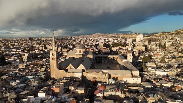 wide aerial drone shot of the Umayyad Mosque in Damascus, showing the entire historic complex and the dense Old City under a dramatic cloudy sky, UNESCO World Heritage site in the heart of Damascus
