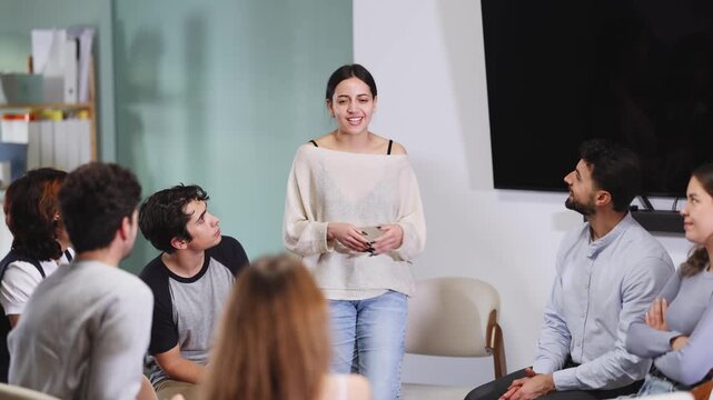 Group of interested students listening to young woman speaking in standing position in bright room