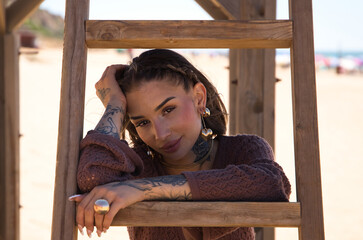 A beautiful young woman in a brown dress rests her arms on the steps of the wooden ladder of the...