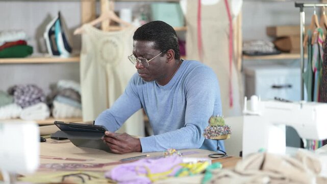 African American man tailor creates sketch of dress on tablet, draws and visualizes model of clothing using computer technology. Software for drawing and visualization