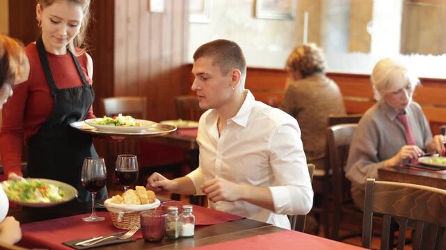 Young couple enjoying relaxed dinner served by a smiling young woman in a warm atmosphere